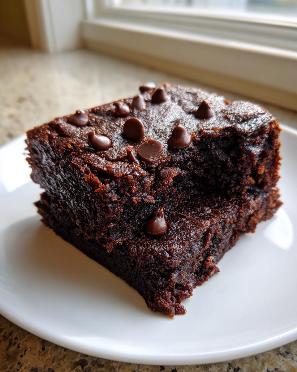 Close-up of a dense, rich slice of sweet potato brownies topped with chocolate chips on a white plate.