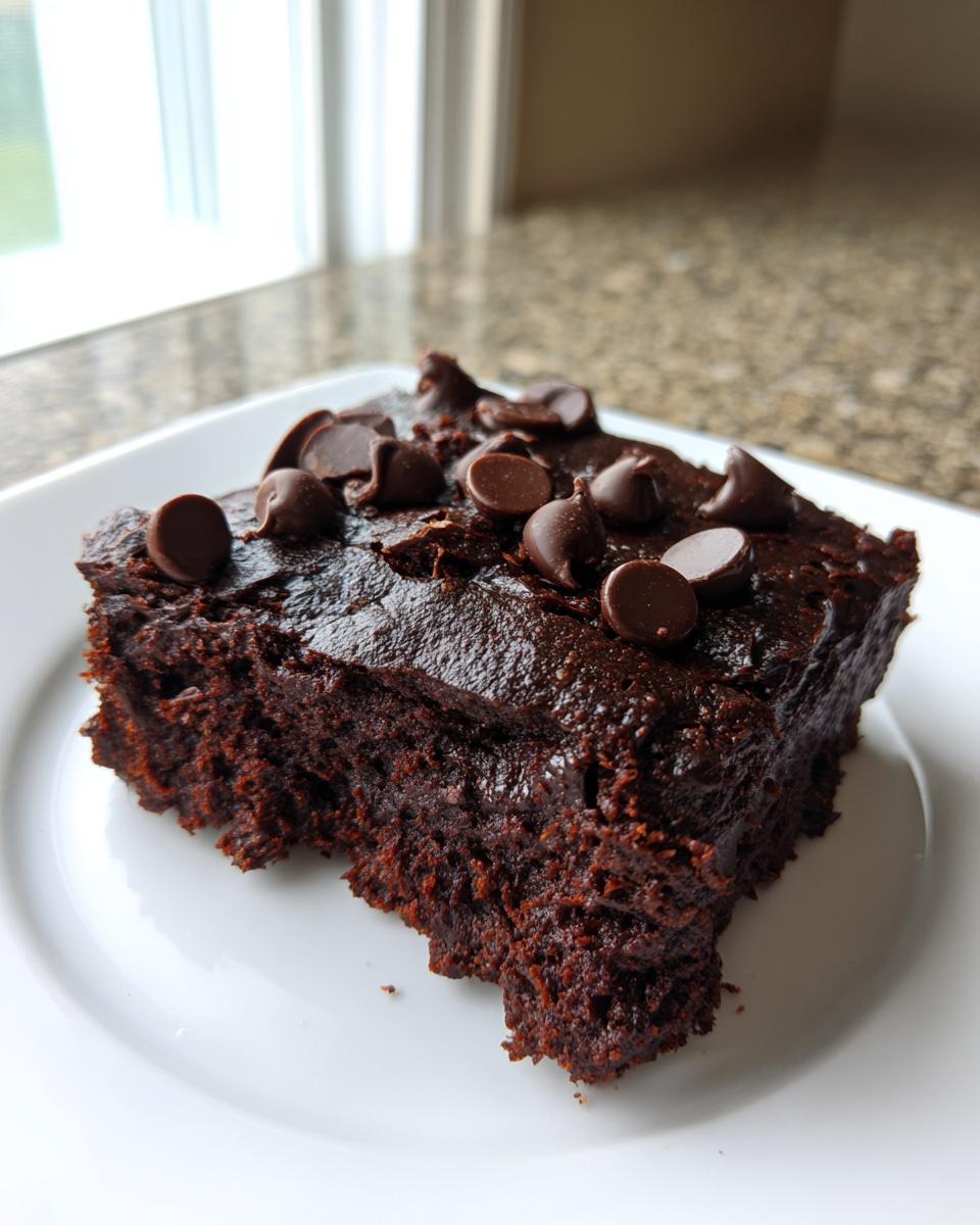 A close-up of a rich, dark slice of sweet potato brownies topped with chocolate chips on a white plate.
