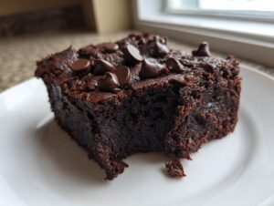 A close-up of a rich, dark, fudgy slice of sweet potato brownies topped with chocolate chips on a white plate.