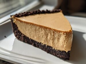 A close-up slice of no bake peanut butter pie with a thick, creamy filling and dark chocolate crust.