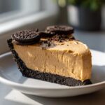 A thick slice of no bake peanut butter pie with a dark chocolate cookie crust, topped with whole and crushed cookies.
