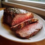 Close-up of a perfectly roasted beef tenderloin, sliced to show medium-rare pink center and rosemary crust.