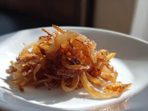 A close-up of deeply golden brown caramelized onions piled high on a white plate.