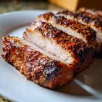 Close-up of thick, juicy slices of pork loin roast with a dark, seasoned crust on a white plate.