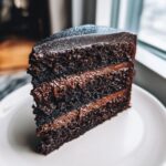 Close-up of a decadent, three-layer chocolate slice of Capricorn cake with dark frosting and silver glitter.