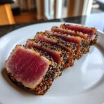 Five slices of sesame crusted Seared Ahi Tuna showing a bright red, rare center on a white plate.