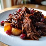 Close-up of tender, shredded cranberry pot roast served with roasted potatoes and whole cranberries.