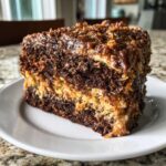 Close-up of a moist slice of german chocolate cake recipe showing dark chocolate layers and coconut pecan frosting.