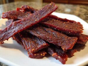 A pile of dark red, seasoned venison jerky strips sprinkled with visible red pepper flakes.