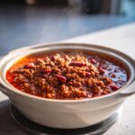 Close-up of rich, steaming crockpot chili filled with ground meat and kidney beans in a white ceramic slow cooker insert.