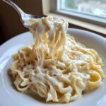 A fork lifts fettuccine coated in rich, creamy homemade alfredo sauce, showing a dramatic cheese pull.