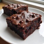 Two rich, fudgy sweet potato brownies topped with chocolate chips resting on a white plate.