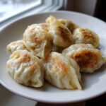 A close-up of several golden-brown pan-fried Traditional Chinese Dumplings served on a white plate.