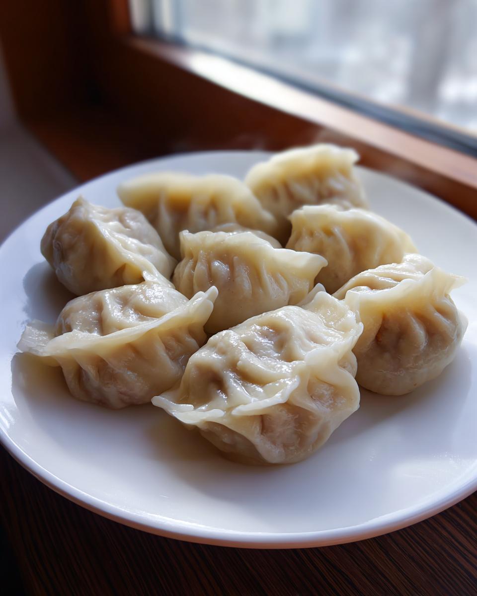 A close-up of several perfectly pleated Traditional Chinese Dumplings served on a white plate near a window.