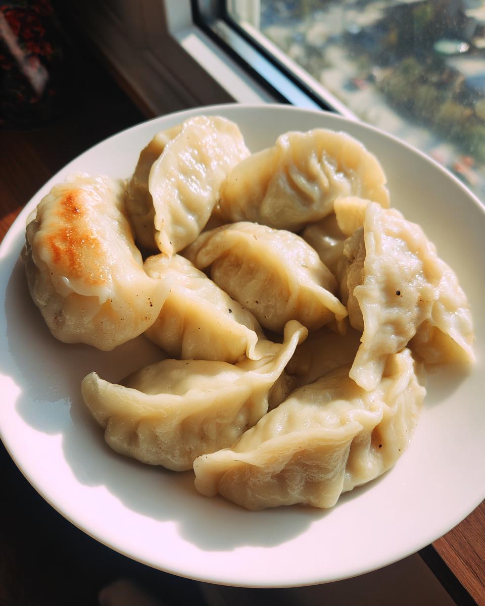 A white plate filled with freshly cooked Traditional Chinese Dumplings, some showing light browning from pan-frying.