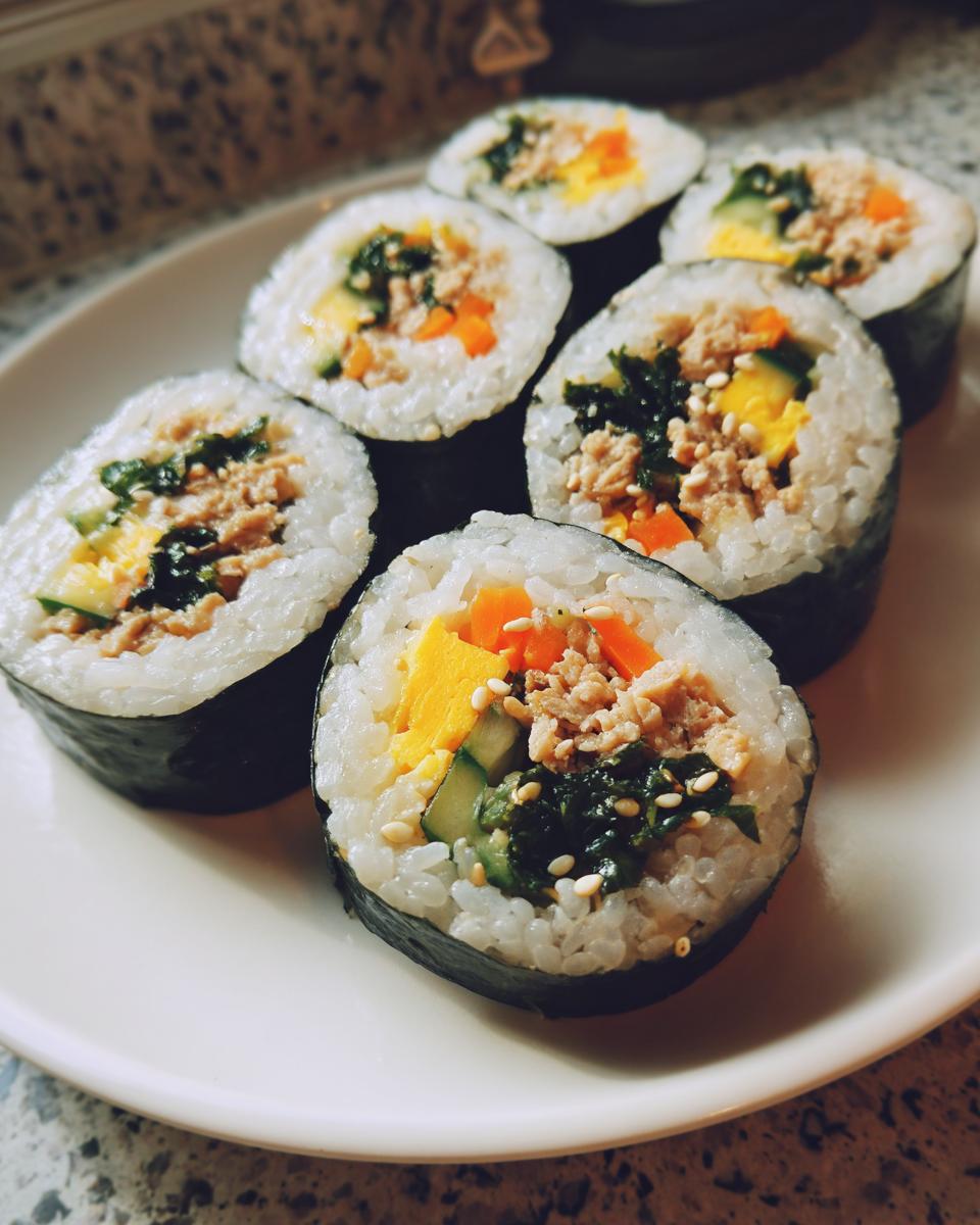 Close-up of several slices of tuna kimbap arranged on a white plate, showing rice, seaweed, tuna, egg, and vegetables.