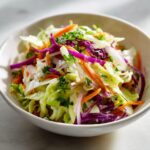 Close-up of a vibrant cabbage salad featuring shredded green and red cabbage, carrots, and parsley in a white bowl.