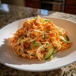 A bright, creamy orange kani salad mixed with shredded white ingredients and thick slices of fresh cucumber.