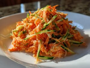 A mound of creamy, bright orange kani salad mixed with julienned cucumber slices on a white plate.
