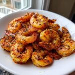 A close-up of perfectly cooked, seasoned air fryer frozen shrimp piled high in a white bowl.