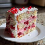 A tall slice of moist cherry cake layered with pink cream filling and topped with white frosting and candied cherries.