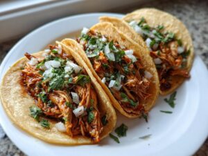 Three soft corn tortillas filled with shredded, saucy chicken, topped with diced white onion and fresh cilantro for amazing chicken tacos.