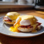 Two servings of classic eggs benedict on an English muffin, topped with poached eggs and rich hollandaise sauce.