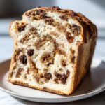 A thick slice of homemade raisin bread showing a swirl of cinnamon sugar and plump raisins throughout the soft crumb.