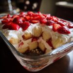 Close-up of a delicious strawberry shortcake trifle in a glass dish, showing layers of sponge cake, whipped cream, and fresh strawberries.