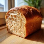 A close-up of a freshly baked whole wheat bread loaf, showing its golden crust and soft, airy crumb texture.