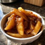 Close-up of thick, glossy apple pie filling recipe slices coated in cinnamon sugar sauce in a white bowl.