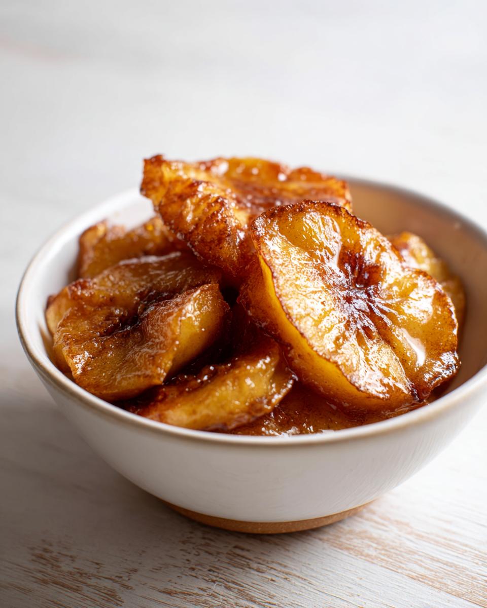 Close-up of caramelized, glistening slices of baked apple served in a small white bowl.