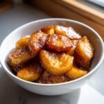 Close-up of sweet, caramelized baked apple slices coated in cinnamon sugar syrup in a white bowl.