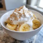 A white bowl filled with creamy banana ice cream, topped with fresh banana slices and cinnamon.