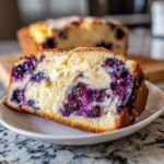 Close-up of a moist slice of Blueberry Cream Cheese Bread showing bright purple blueberries and a cream cheese swirl.