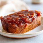 Close-up of a slice of spiced cake generously topped with glistening homemade apple butter.