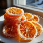 A stack and pile of bright orange candied orange slices heavily coated in sparkling white sugar.