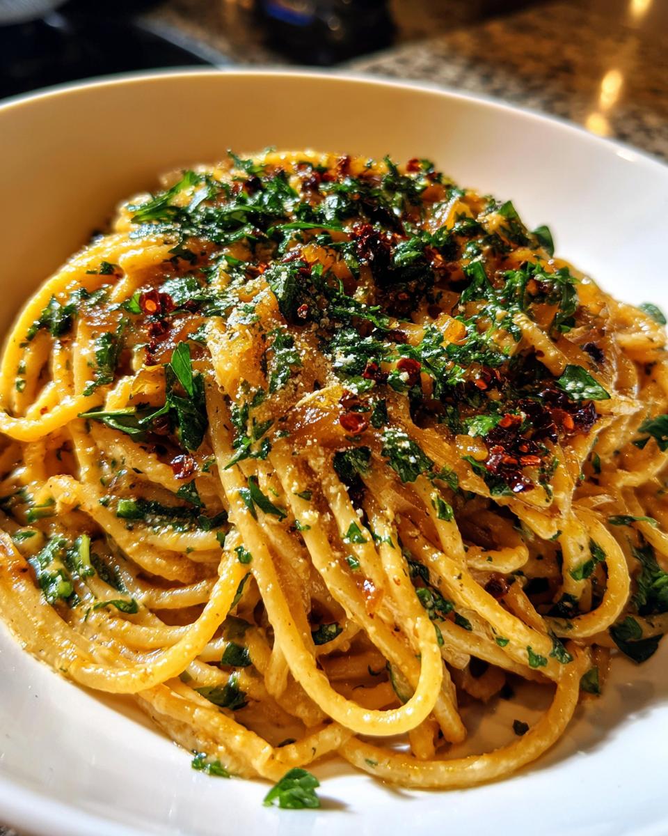 A close-up of creamy caramelized onion pasta topped with fresh parsley, Parmesan, and red pepper flakes.