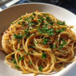 Close-up of a bowl of creamy caramelized onion pasta topped with fresh parsley and red pepper flakes.
