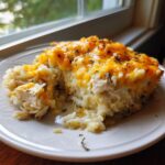A close-up of a serving of creamy chicken and rice casserole topped with melted cheddar cheese and herbs.