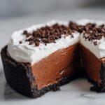Cross-section view of a decadent chocolate mousse pie showing the dark crust, rich filling, and whipped cream topping sprinkled with crumbs.