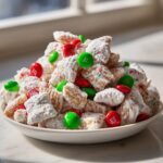 A mound of powdered sugar-coated Christmas puppy chow mixed with red and green M&M's in a white bowl.