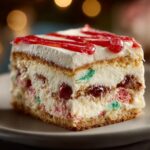 Close-up of a slice of christmas tree cheesecake layered with cream, cake, and festive red and green candied fruit.