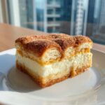 A square slice of rich churro cheesecake with a creamy filling and cinnamon sugar topping.