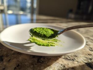 A spoonful of vibrant, bright green cilantro lime sauce being held over a white plate.