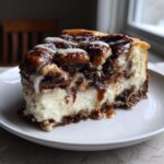 A decadent slice of cinnamon roll cheesecake featuring a creamy base, cinnamon swirls, and drizzled with icing.