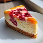 A perfect slice of cranberry orange cheesecake with a graham cracker crust, topped with swirls of cranberry and orange pieces.
