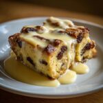A close-up of a rich slice of bread pudding recipe topped generously with vanilla custard sauce.
