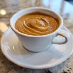 Close-up of creamy peanut sauce with a swirl pattern, served in a small white espresso cup and saucer.