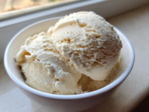 Close-up of two scoops of creamy, light-colored protein ice cream served in a small white bowl.